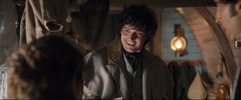 Movie still from “The Personal History of David Copperfield” (2019), directed by Armando Iannucci – A man in a jacket smiles for the camera; Medium shot, Over the shoulder angle