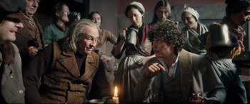 Movie still from “The Personal History of David Copperfield” (2019), directed by Armando Iannucci – A group of people sitting around a table with a lit candle; Medium shot, Over the shoulder angle