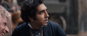 Movie still from “The Personal History of David Copperfield” (2019), directed by Armando Iannucci – A person wearing a suit and tie; Close Up shot, Over the shoulder angle