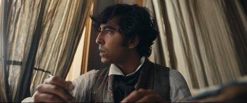 Movie still from “The Personal History of David Copperfield” (2019), directed by Armando Iannucci – A man with long black hair wearing a vest and a tie; Close Up shot, Over the shoulder angle