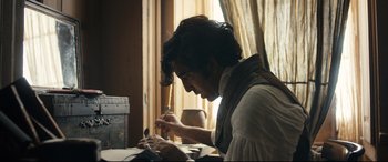 Movie still from “The Personal History of David Copperfield” (2019), directed by Armando Iannucci – A man writing on a piece of paper at a table; Medium shot, Low angle