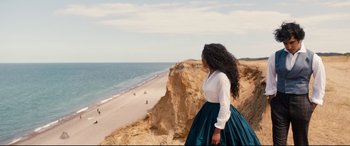 Movie still from “The Personal History of David Copperfield” (2019), directed by Armando Iannucci – A woman standing on top of a cliff looking out at the ocean; Extreme Wide shot, High angle
