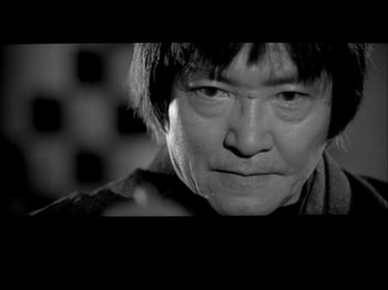 Movie still from “The Pillow Book” (1995), directed by Peter Greenaway – A black - and - white photo of a man with a short haircut; Close Up shot, Low angle