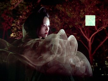 Movie still from “The Pillow Book” (1995), directed by Peter Greenaway – A woman in a white dress is standing in front of a tree; Medium shot, Low angle