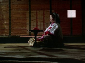 Movie still from “The Pillow Book” (1995), directed by Peter Greenaway – A girl sitting on the ground with a candle in her hand; Wide shot, High angle
