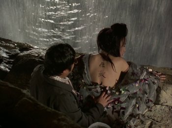 Movie still from “The Pillow Book” (1995), directed by Peter Greenaway – A man and a woman sitting on a rock in front of a waterfall; Medium shot, High angle