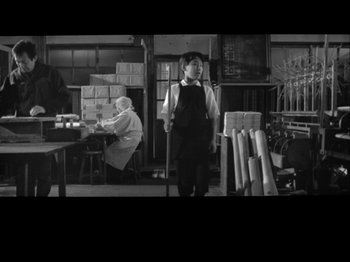 Movie still from “The Pillow Book” (1995), directed by Peter Greenaway – A man standing in front of a table in a room; Wide shot, Low angle