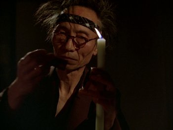 Movie still from “The Pillow Book” (1995), directed by Peter Greenaway – An older man holding a candle in front of his face; Close Up shot, Low angle