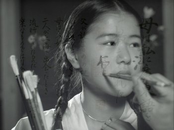 Movie still from “The Pillow Book” (1995), directed by Peter Greenaway – A young girl with pigtails is writing on a piece of paper; Extreme Close Up shot, Low angle