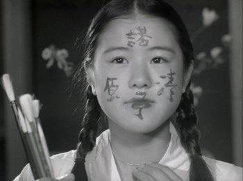 Movie still from “The Pillow Book” (1995), directed by Peter Greenaway – A young girl with a face paint holding a paintbrush in her hand; Close Up shot, High angle