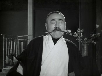 Movie still from “The Pillow Book” (1995), directed by Peter Greenaway – An old photo of a man holding a stick in his mouth; Medium shot, Low angle