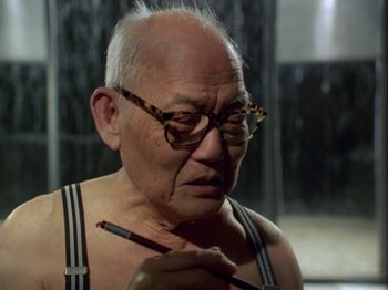 Movie still from “The Pillow Book” (1995), directed by Peter Greenaway – An older man wearing glasses and holding a pencil; Close Up shot, Over the shoulder angle