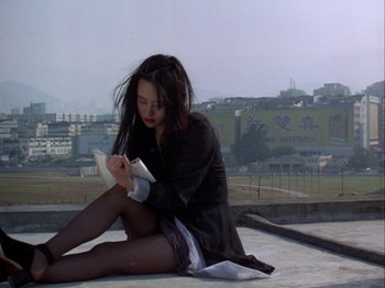Movie still from “The Pillow Book” (1995), directed by Peter Greenaway – A woman sitting on the ground writing on a book; Medium shot, High angle