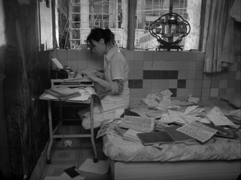 Movie still from “The Pillow Book” (1995), directed by Peter Greenaway – A woman sitting at a desk in a room with papers; Wide shot, High angle