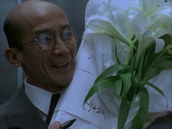 Movie still from “The Pillow Book” (1995), directed by Peter Greenaway – A man in a suit holding a bouquet of white flowers; Close Up shot, Over the shoulder angle