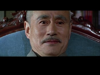 Movie still from “The Pillow Book” (1995), directed by Peter Greenaway – An older man with a mustache sitting in a chair; Close Up shot, High angle
