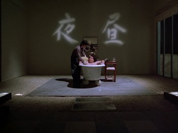 Movie still from “The Pillow Book” (1995), directed by Peter Greenaway – A person is sitting in a tub in a room; Wide shot, High angle