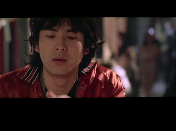 Movie still from “The Pillow Book” (1995), directed by Peter Greenaway – A man in a red jacket is looking down at his chin; Close Up shot, Low angle