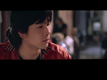 Movie still from “The Pillow Book” (1995), directed by Peter Greenaway – A young man in a red shirt looking to his left; Close Up shot, High angle
