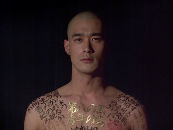 Movie still from “The Pillow Book” (1995), directed by Peter Greenaway – A bald man with tattoos on his chest and shoulders; Close Up shot, Low angle