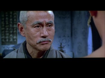 Movie still from “The Pillow Book” (1995), directed by Peter Greenaway – An older man with a mustache is looking at the camera; Close Up shot, Over the shoulder angle