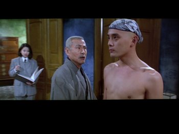Movie still from “The Pillow Book” (1995), directed by Peter Greenaway – A man standing next to another man in front of a woman; Medium shot, Over the shoulder angle