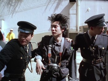 Movie still from “The Pillow Book” (1995), directed by Peter Greenaway – A group of men standing next to each other on a street; Medium shot, Low angle