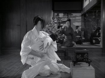 Movie still from “The Pillow Book” (1995), directed by Peter Greenaway – A woman holding a baby while sitting on the ground; Wide shot, High angle