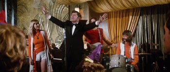 Movie still from “The Poseidon Adventure” (1972), directed by Ronald Neame – A man in a black suit singing into a microphone; Medium shot, Low angle