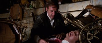 Movie still from “The Poseidon Adventure” (1972), directed by Ronald Neame – A man in a black suit and white shirt is cutting a man's face; Medium shot, Low angle