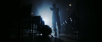 Movie still from “The Prince” (2014), directed by Brian A. Miller – A man standing in a room holding a cell phone; Wide shot, Low angle