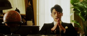 Movie still from “The Prince” (2014), directed by Brian A. Miller – A man in a black suit and white shirt is praying in front of a desk; Close Up shot, Low angle