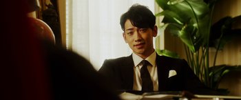 Movie still from “The Prince” (2014), directed by Brian A. Miller – A man in a suit and tie sitting in front of a window; Close Up shot, Over the shoulder angle