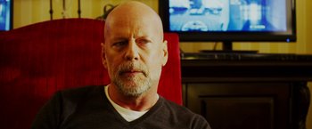 Movie still from “The Prince” (2014), directed by Brian A. Miller – A bald man with a goatee sitting in front of a television; Close Up shot, Over the shoulder angle