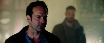 Movie still from “The Prince” (2014), directed by Brian A. Miller – A man standing next to another man in a dark room; Close Up shot, Over the shoulder angle