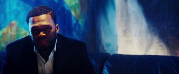 Movie still from “The Prince” (2014), directed by Brian A. Miller – A man sitting on a couch in front of a painting; Close Up shot, Low angle