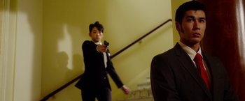Movie still from “The Prince” (2014), directed by Brian A. Miller – A man in a suit holding a gun in his hand; Medium shot, Over the shoulder angle