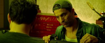 Movie still from “The Prince” (2014), directed by Brian A. Miller – A man in a green hat is holding a wrench; Close Up shot, Over the shoulder angle