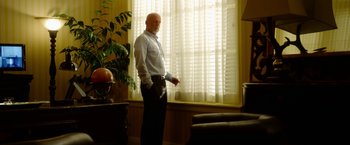 Movie still from “The Prince” (2014), directed by Brian A. Miller – A man standing in front of a window in a living room; Medium shot, Low angle