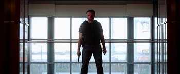 Movie still from “The Prince” (2014), directed by Brian A. Miller – A man holding a knife in front of a large window; Medium shot, Low angle