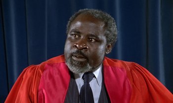 Movie still from “The Professional” (1981), directed by Georges Lautner – An older man wearing a red and black robe; Close Up shot, Low angle