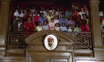 Movie still from “The Professional” (1981), directed by Georges Lautner – A large group of people sitting on a stage; Wide shot, High angle
