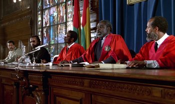 Movie still from “The Professional” (1981), directed by Georges Lautner – A group of men sitting at a table in front of stained glass windows; Medium shot, Low angle