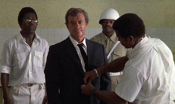 Movie still from “The Professional” (1981), directed by Georges Lautner – A man in a black suit and a man in a white helmet; Medium shot, Over the shoulder angle