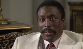 Movie still from “The Professional” (1981), directed by Georges Lautner – A man in a white suit and a pink tie; Close Up shot, Low angle