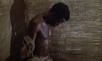 Movie still from “The Professional” (1981), directed by Georges Lautner – A man with a bare torso is standing in a room; Medium shot, High angle