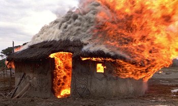 Movie still from “The Professional” (1981), directed by Georges Lautner – A house on fire with a thatched roof; Extreme Wide shot, Low angle