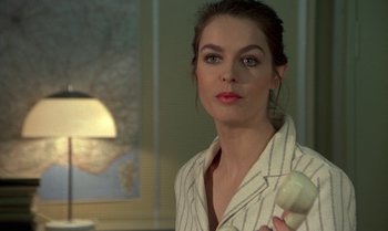 Movie still from “The Professional” (1981), directed by Georges Lautner – A woman holding a remote control in her hand; Close Up shot, Over the shoulder angle