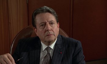 Movie still from “The Professional” (1981), directed by Georges Lautner – A person wearing a suit and tie; Close Up shot, Over the shoulder angle