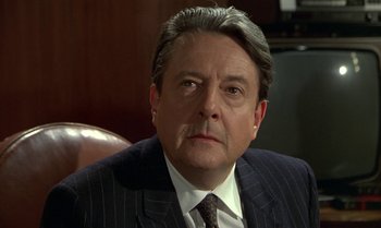 Movie still from “The Professional” (1981), directed by Georges Lautner – A person wearing a suit and tie; Close Up shot, Over the shoulder angle